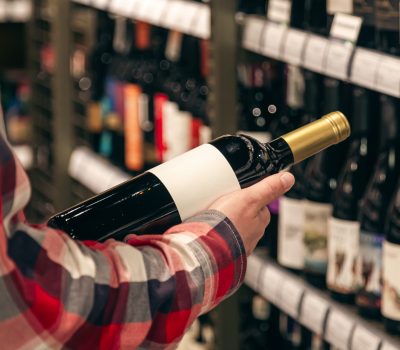 A man holding a wine bottle in a liquor wine shop, choosing the right wine from all the variations of wine bottles on the shelves.