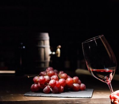 Woman holds glass of wine before bunch of grape lying on black p